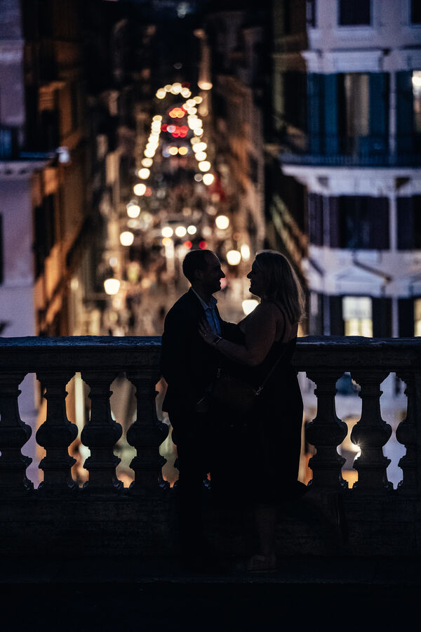 Low-key portrait of newly-engaged couple on the Spanish Steps in Rome at dark with via Condotti in the background fully lit