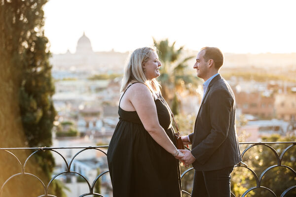Couple holding hands in the warm sunset light on the Terrazza Belvedere in Rome before their surprise wedding proposal