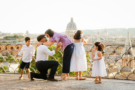 Future wife kissing his proposing husband to be during a surprise wedding proposal with their 3 kids on the Terrazza Belvedere in Rome