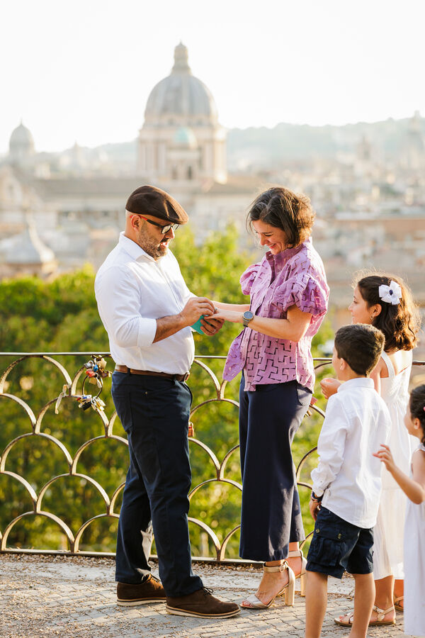 Husband to be putting the engagement ring on his future wife with their 3 kids around them on the Terrazza Belvedere in Rome