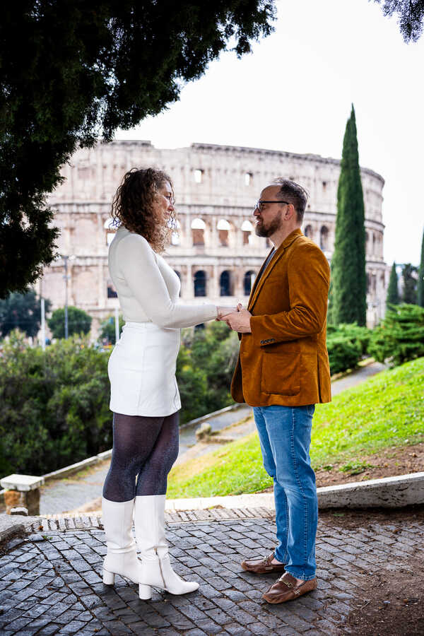 Couple holding hands with the Colosseum in the background, during their surprise proposal shoot in Rome