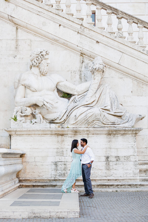Newly-engaged couple standing in front of the Tiber God statue on the Capiteoline Hill during their engagement photo session in Rome