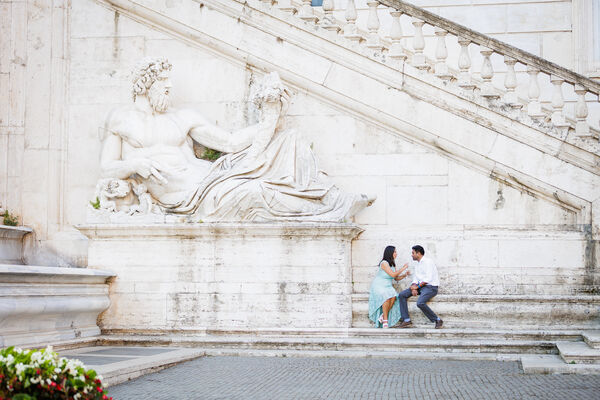 Newly-engaged couple sitting by the Tiber God statue on the Capiteoline Hill during their engagement photo session in Rome
