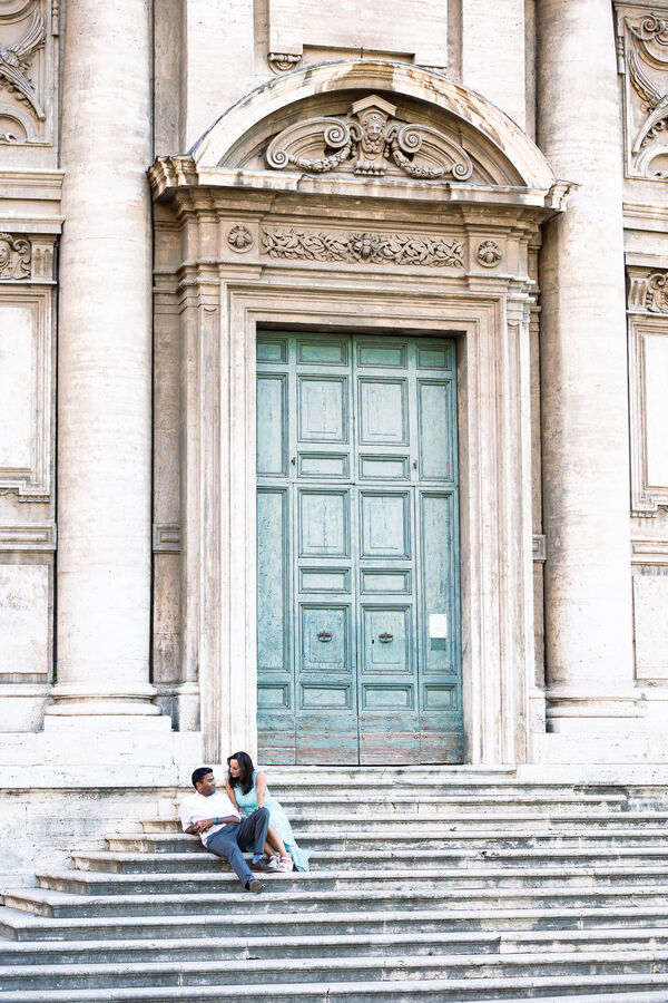 Newly-engaged couple sitting on the staircase to Chiesa Santi Luca e Martina martiri in Rome