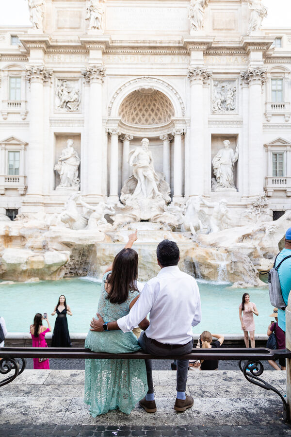 Newly-engaged couple sitting looking at the Trevi Fountain in Rome