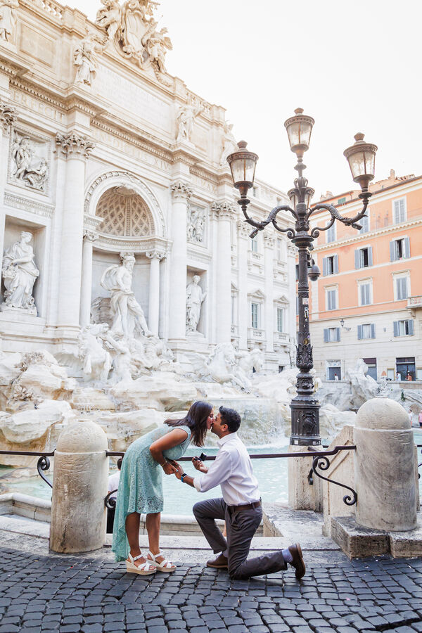 Newly-engaged couple kissing during their surprise proposal photo shoot at the Trevi Fountain