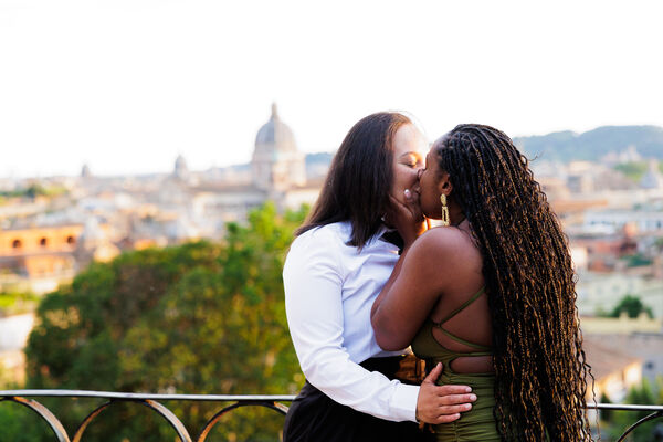 Lesbian couple kissing during their surprise proposal in Rome on the Terrazza Belvedere at sunset