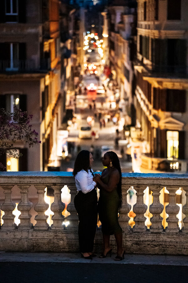 Newly-engaged couple holding each other on the Spanish Steps with Via Condotti in the background