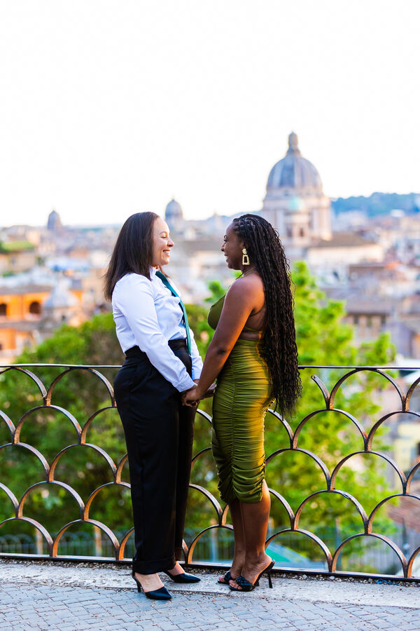 Gay female couple holding hands on the Terrazza Belvedere during their surprise marriage proposal at sunset in Rome