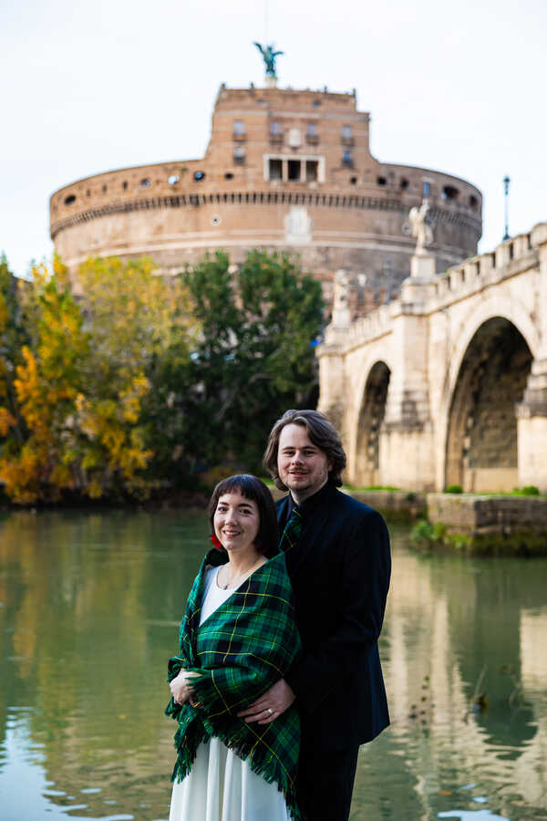 A Sposi Novelli couple posing for the camera on the Tiber riverbank with Castel Sant'Angelo in the background