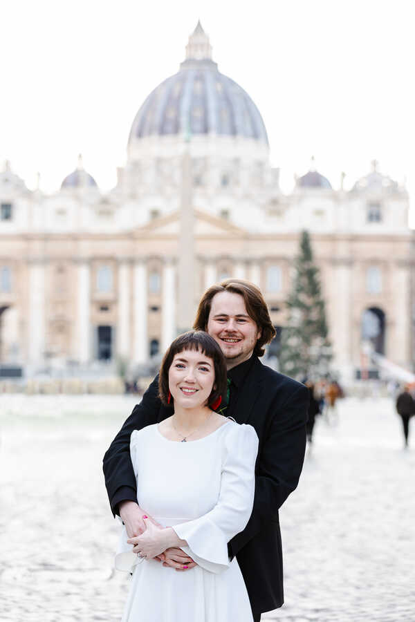 Radiant newly-wed couple holding each other in Via della Conciliazione with Saint Peter's Basilica in the background